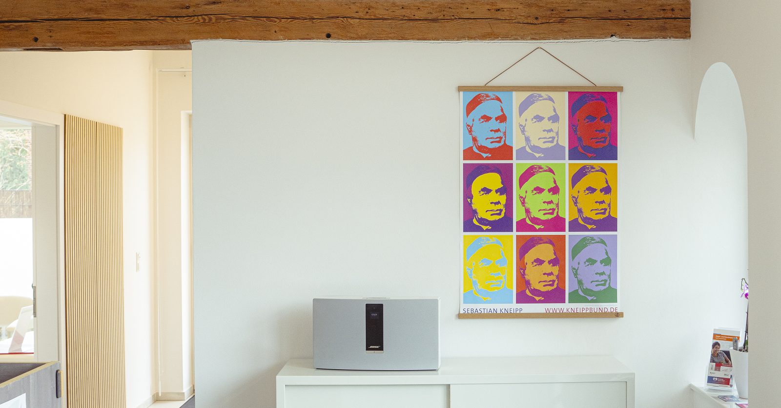 Empfangsbereich unter einem Holzbalken, an der Wand ein farbiges Poster von Sebastian Kneipp